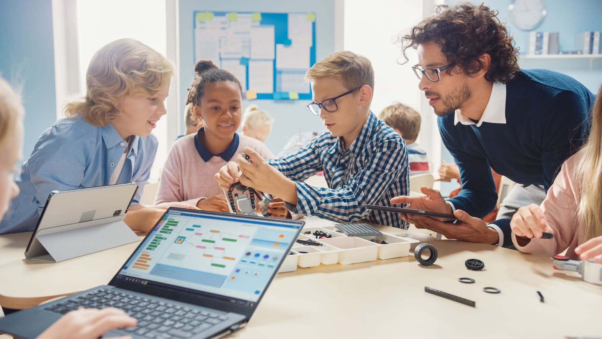 Children and an adult working with laptops in a classroom